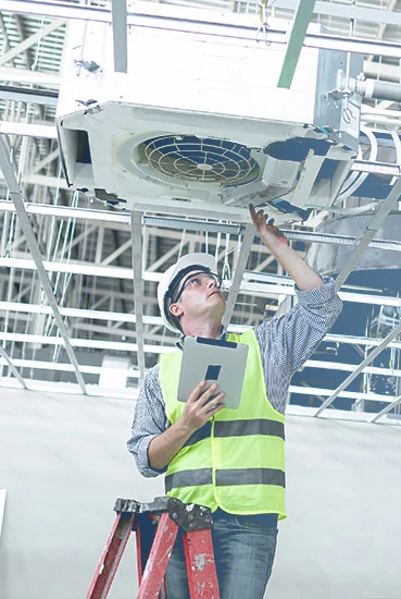 Technician inspecting a ceiling-mounted ventilation and air conditioning unit